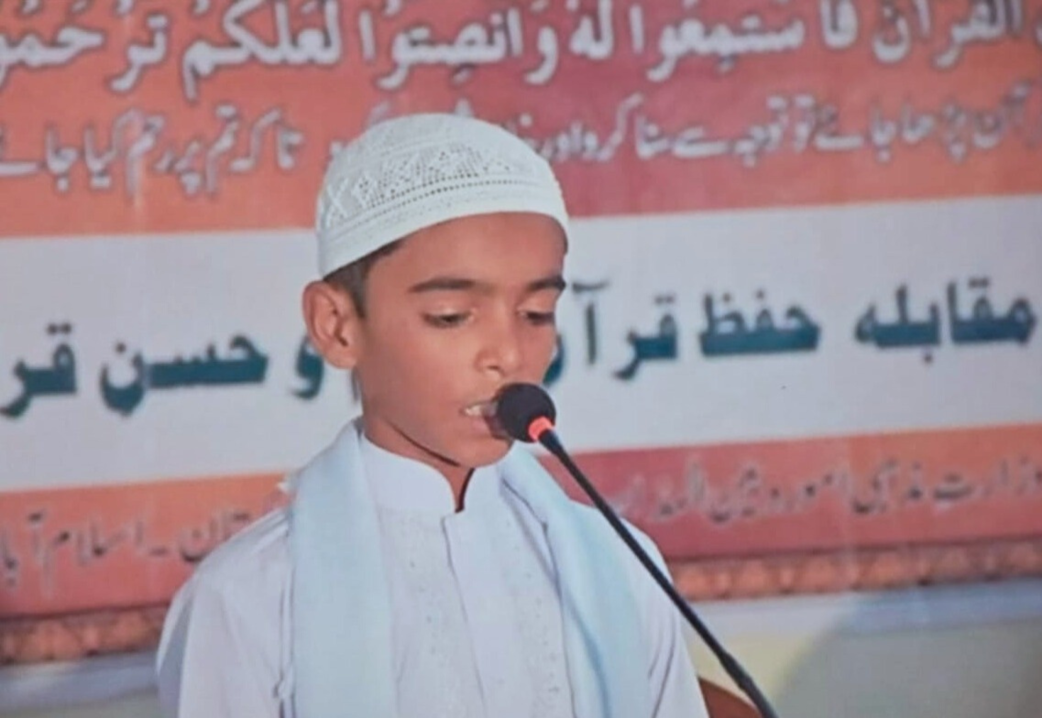 Student reciting the Quran into a microphone during a recitation competition